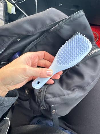 Reviewer holding mini tangle teezer adjacent to bag
