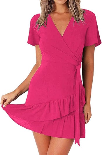 Model wearing hot pink short sleeve, V-neck dress with side wrap tie and bottom two-tier ruffles on a white background