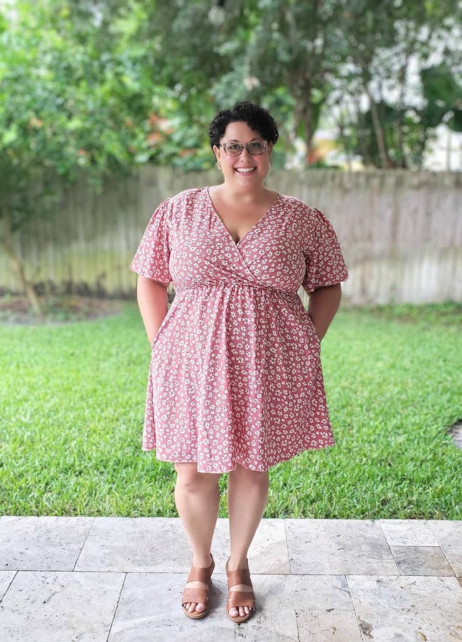 Reviewer standing outdoors smiling, wearing a floral patterned dress with short sleeves and sandals