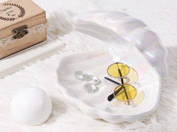 A shiny clamshell dish with yellow-lensed glasses and jewelry with the removable pearl next to it