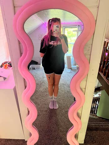 reviewer taking pic in front of pink wavy mirror
