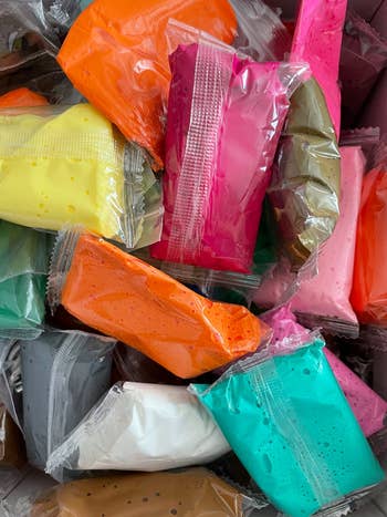 Packets of colorful air-dry clay stacked together, showcasing a assortment  of vibrant crafting options