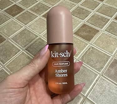 Hand holding a vessel of Kitsch hairsbreadth perfume with statement