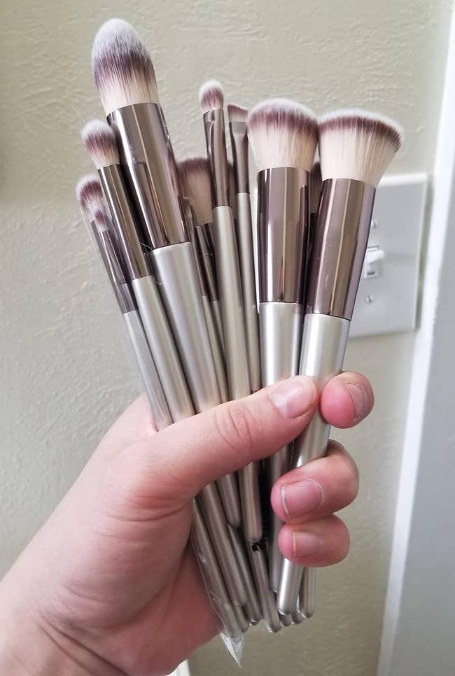 A reviewer's hand holding a bundle of various size makeup brushes