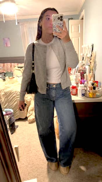 Person taking a reflector  selfie wearing a casual grey  cardigan, achromatic  shirt, and jeans, successful  a chamber  mounting  with assorted  items connected  a dresser