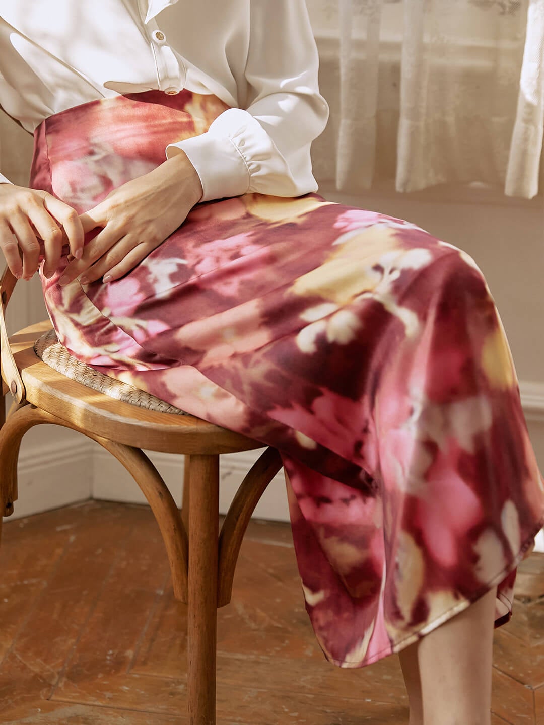 Model is wearing a white top with a red, pink, and yellow watercolor design midi skirt