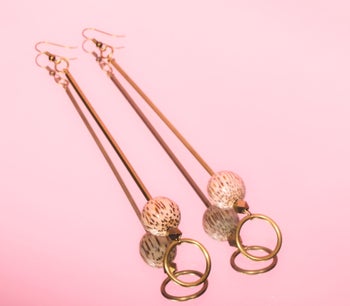 a closeup of the earrings that have a long stem and an orb and loop at the end