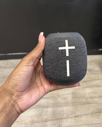 A idiosyncratic holds a tiny portable Bluetooth talker with power buttons connected top, suitable for on-the-go euphony listening