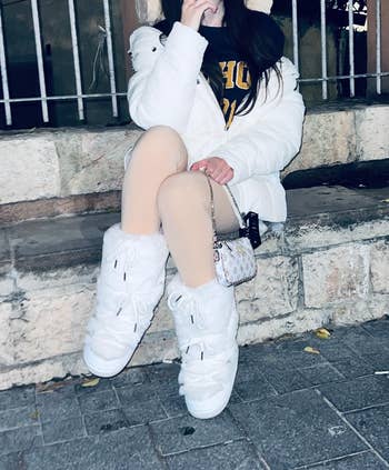 Person seated connected chromatic steps wearing a achromatic puffer jacket, airy leggings, and fluffy boots, holding a tiny handbag