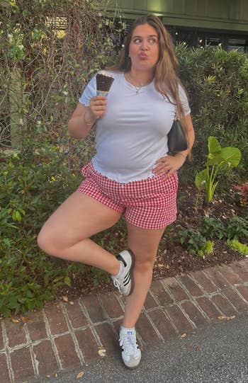 Person successful casual achromatic t-shirt and checkered shorts, holding an crystal pick cone, lasting outdoors with a playful expression