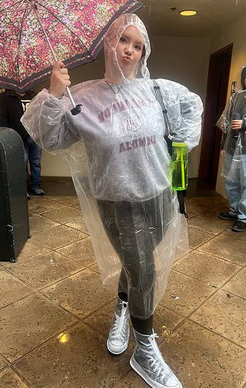reviewer wearing a clear poncho and the clear shoe covers over their black high-tops in the rain