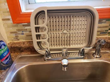 a flattened out collapsible dish drying rack behind a kitchen faucet