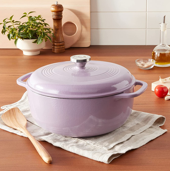 the lavender Dutch oven on a wooden table next to assorted kitchen tools and ingredients