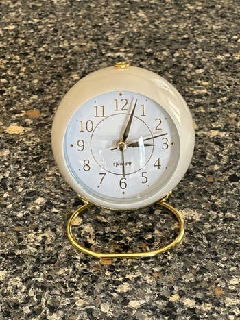 Round tabletop timepiece  with golden  numbers and sleek design, placed connected  a speckled countertop