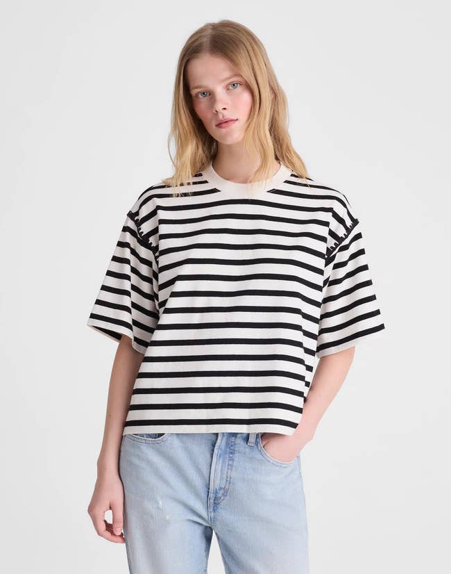 Person in a black and white striped t-shirt and light blue jeans, posing for a fashion shoot