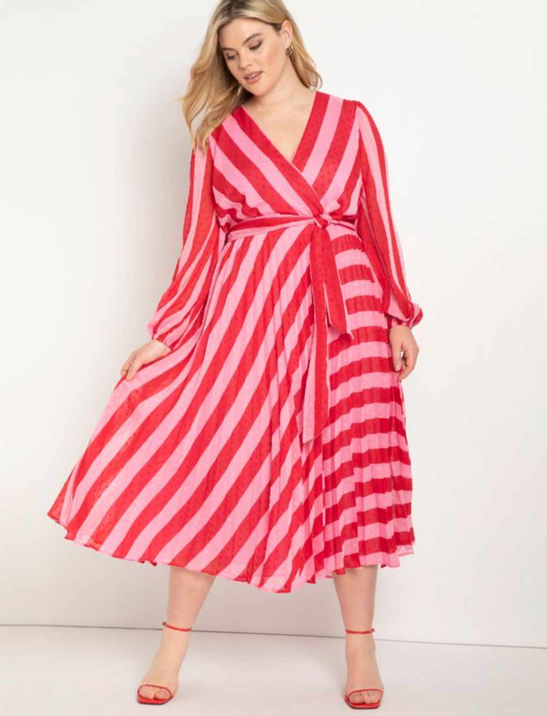 Model wearing midi-length long sleeve hot pink and light pink striped dress with tie waist and pleated skirt