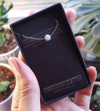 reviewer photo of them holding a black box with a gold and opal-pendant choker necklace in it
