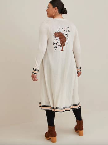 model in calf-length white cardigan with stripe trim and leopard and leopard spots embroidered on back