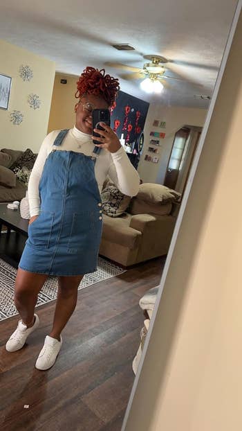 Reviewer in mirror selfie wearing a denim overall dress and white long-sleeve mock neck bodysuit, accessorized with a headwrap and white sneakers