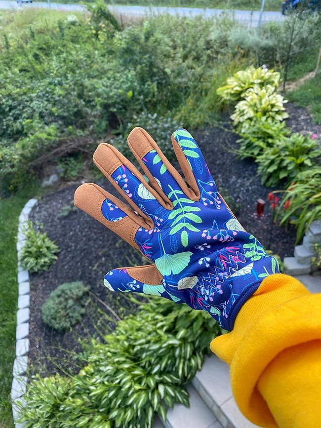 Person wearing a patterned garden glove, with a landscaped yard in the background