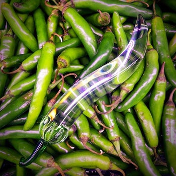 Glass chili pepper dildo on top of actual peppers
