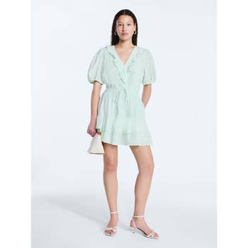 Person modeling a short, puff-sleeve, tiered dress with ruffles, holding a small handbag. They wear strappy heels. Fashionable and elegant style