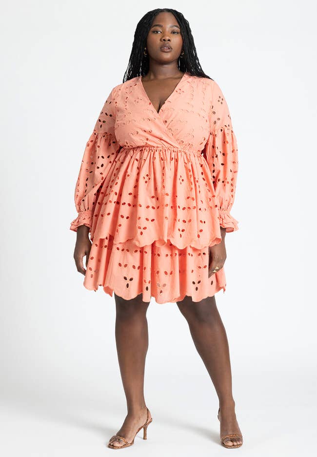 Woman in a peach ruffled dress and clear heels, posing for a fashion-oriented shopping article