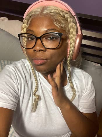 Person wearing headphones, glasses, and a achromatic t-shirt, with braided hair, posing for a selfie