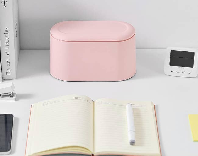 Small pink oval-shaped trash bin with lid on top of a desk 