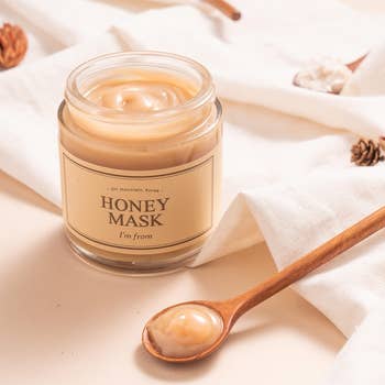Jar of I'm from Honey Mask with a wooden spoon of product beside it, on a fabric surface