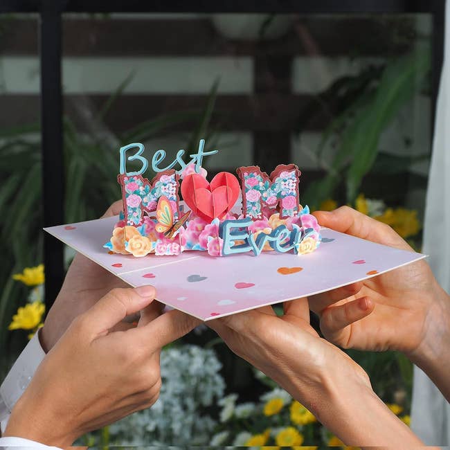 Hands holding a 3D pop-up card with the phrase