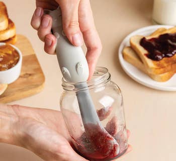 Hand using a cat-shaped knife to scrape jelly out of a jar 