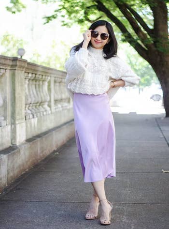 reviewer posing in a textured white blouse and lavender skirt with neutral heels