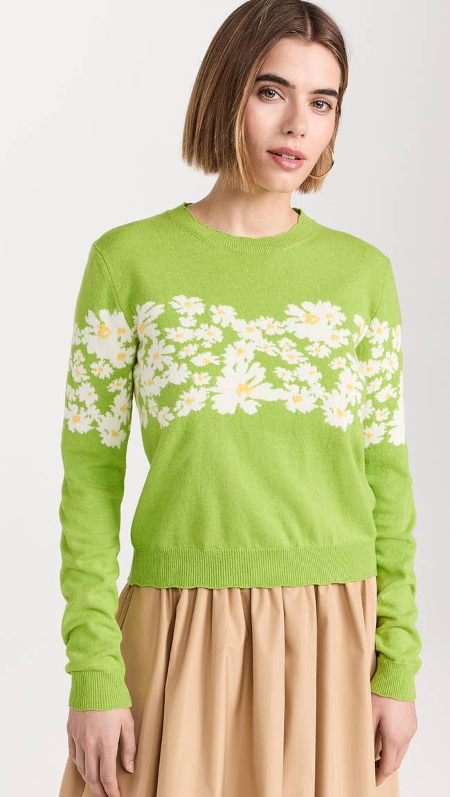 model in a green crewneck sweater with daisies across the chest and upper arms