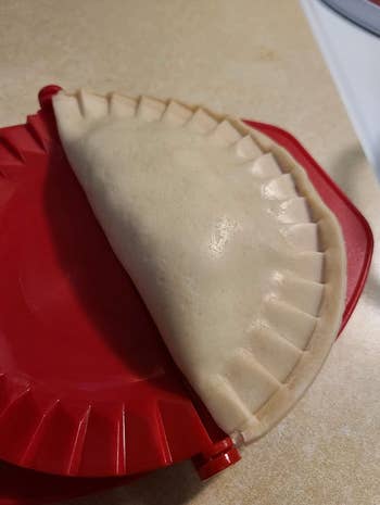 An uncooked empanada in one of the dough presses after being shaped