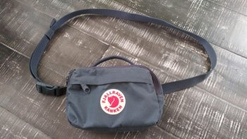 Reviewer image of gray fanny pack with red fox logo in the center and clip strap above on a wooden background