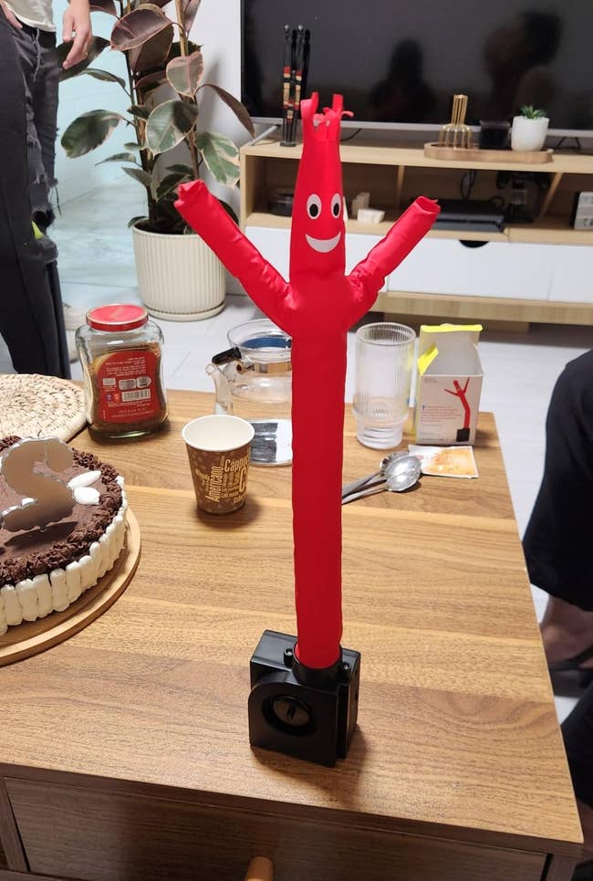 Inflatable red tube man model on a wooden table surrounded by desserts, cups, and decor, suggesting a playful atmosphere