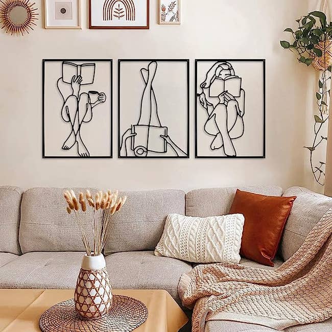 Three metal images of a person reading a book in various positions on a wall above a couch