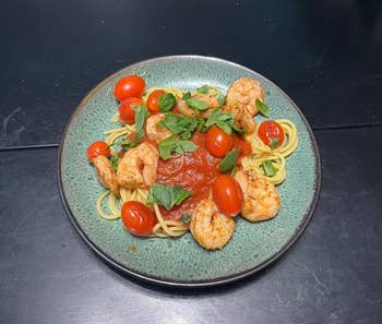 Pasta with shrimp, cherry tomatoes, and caller  basil connected  a plate, presented with a sauce. Perfect for a gourmet eating  experience
