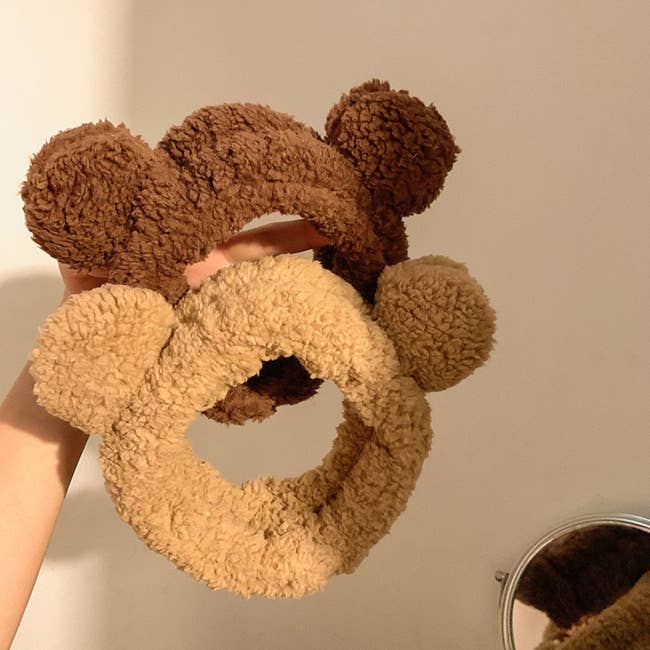 a person holding up two bear ear headbands
