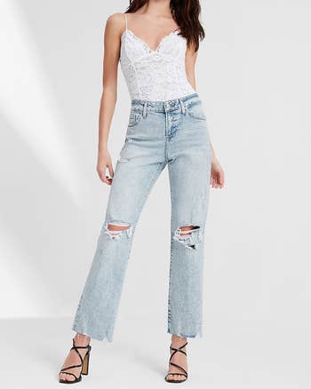 model in slightly acid wash mid rise light blue jeans with raw hem and knee rips