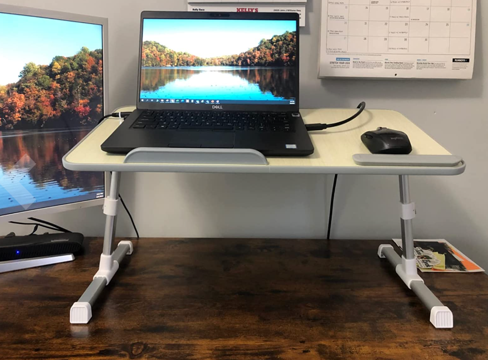 A small white standing desk propped on a real desk elevating a laptop and a mouse 