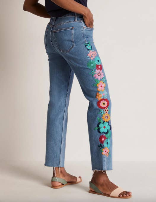 model in frayed hem medium wash jeans with large colorful flowers embroidered along the sides