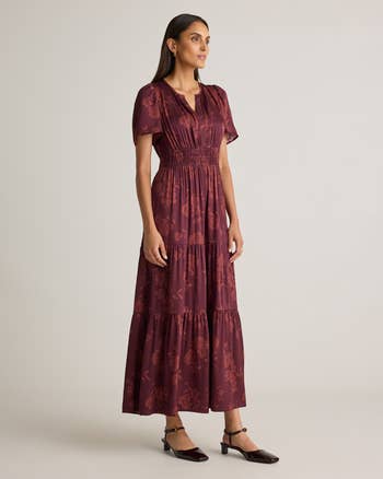 Person in a patterned long dress and flats, posing. The dress has short sleeves and a flowing skirt