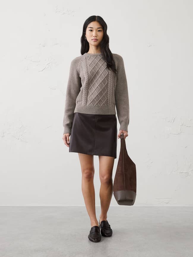 Person wearing a textured sweater and leather skirt, holding a ample  tote bag