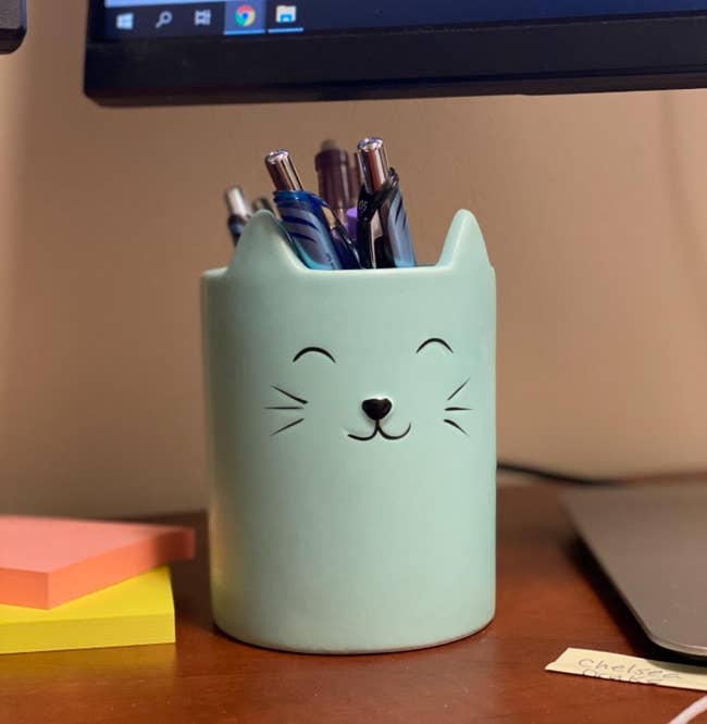 a light green cat-shaped cup with a tiny smiling cat face on it