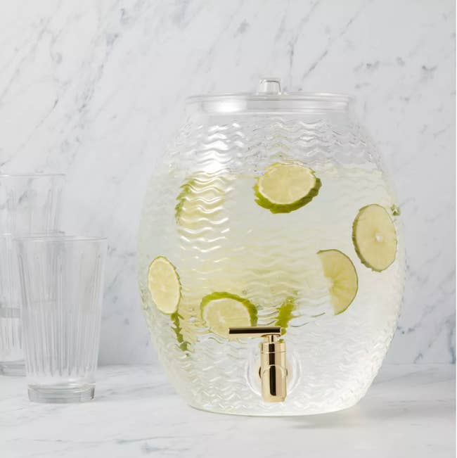 A wave textured rounded clear beverage dispenser with a gold nozzle 