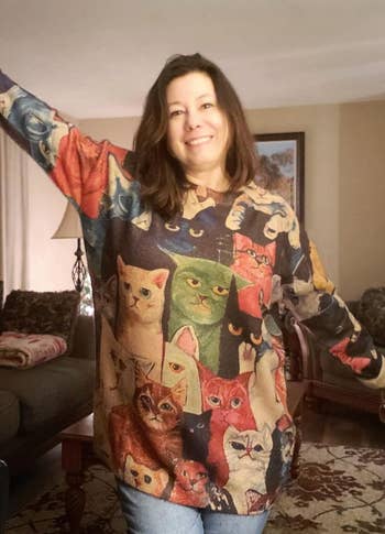 reviewer wearing grumpy cats graphic sweater with arms spread showing design