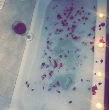 reviewer's tub with roses and bubbles in it, candles around it and the wine holder stuck to the bathroom wall close by