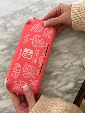 Person holding a Nintendo Switch in a pink case with a pattern design